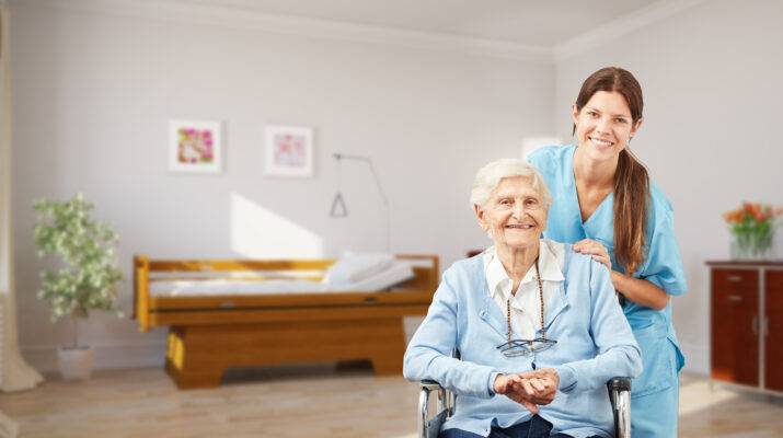 Lächelnde Seniorin im Rollstuhl mit Pflegekraft