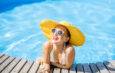 Junge Frau im Badeanzug mit großem gelben Sonnenhut entspannt sich mit einem frischen Getränk am Pool