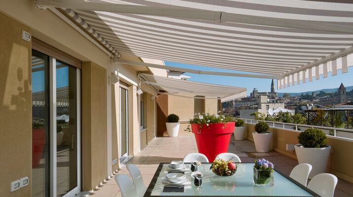 Außenaufnahmen Balkon, unter Markise, mit gläsernem Esstisch im Vordergrund mit Tellern und einer Weintraube
