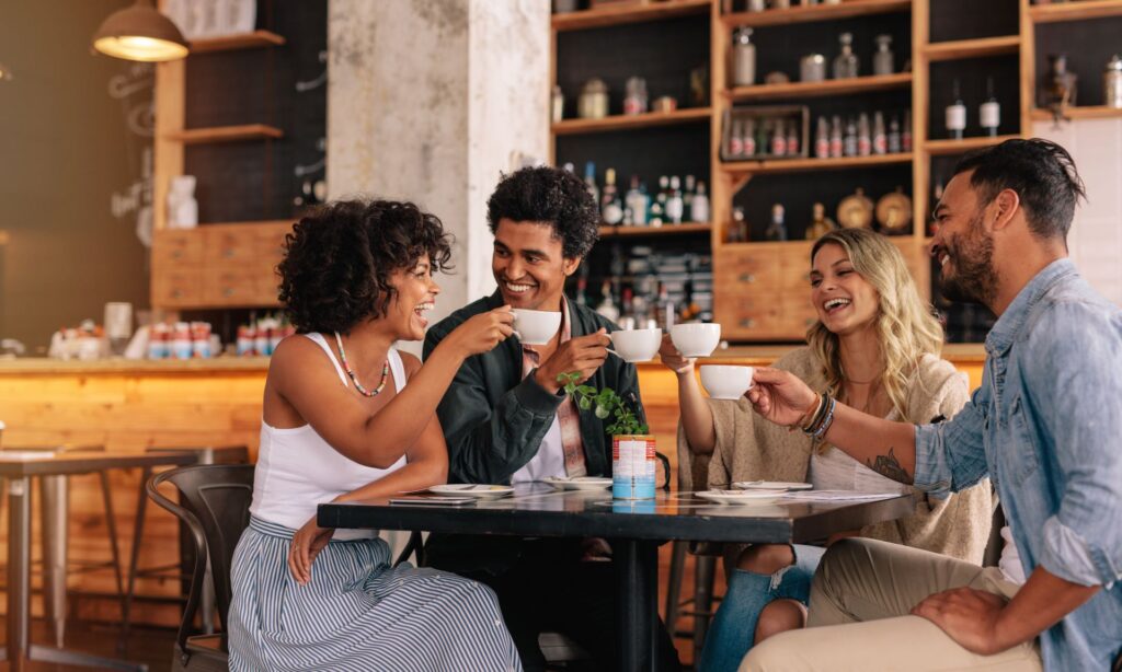 Eine Gruppe von Freunden sitzt in einem gemütlichen Café in Frankfurt, lacht und genießt gemeinsam Kaffee.