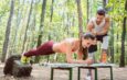 Eine Frau macht unter Anleitung ihres Personal Trainers eine Plank-Übung auf einer Bank im Kölner Stadtwald. Die grüne Umgebung bietet eine ruhige und motivierende Atmosphäre für ein intensives Outdoor-Training.