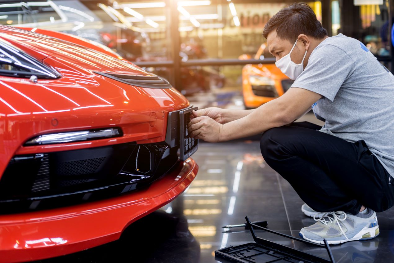 Ein Mann montiert ein Wunschkennzeichen an ein rotes Auto in Mettmann. Perfekt für Fahrzeugzulassung und individuelle Kennzeichen.