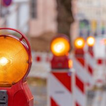 Reihe von gelben Baustellenleuchten mit Warnbaken auf städtischer Straße bei Tageslicht, Fokus auf Vordergrundleuchte