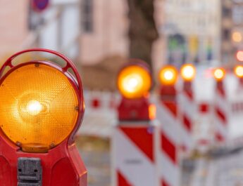 Reihe von gelben Baustellenleuchten mit Warnbaken auf städtischer Straße bei Tageslicht, Fokus auf Vordergrundleuchte