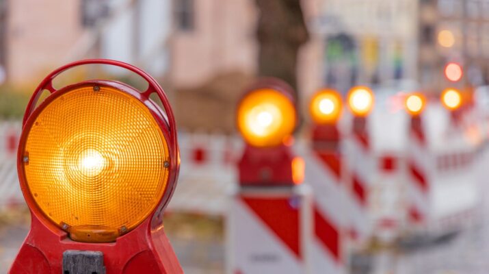 Reihe von gelben Baustellenleuchten mit Warnbaken auf städtischer Straße bei Tageslicht, Fokus auf Vordergrundleuchte