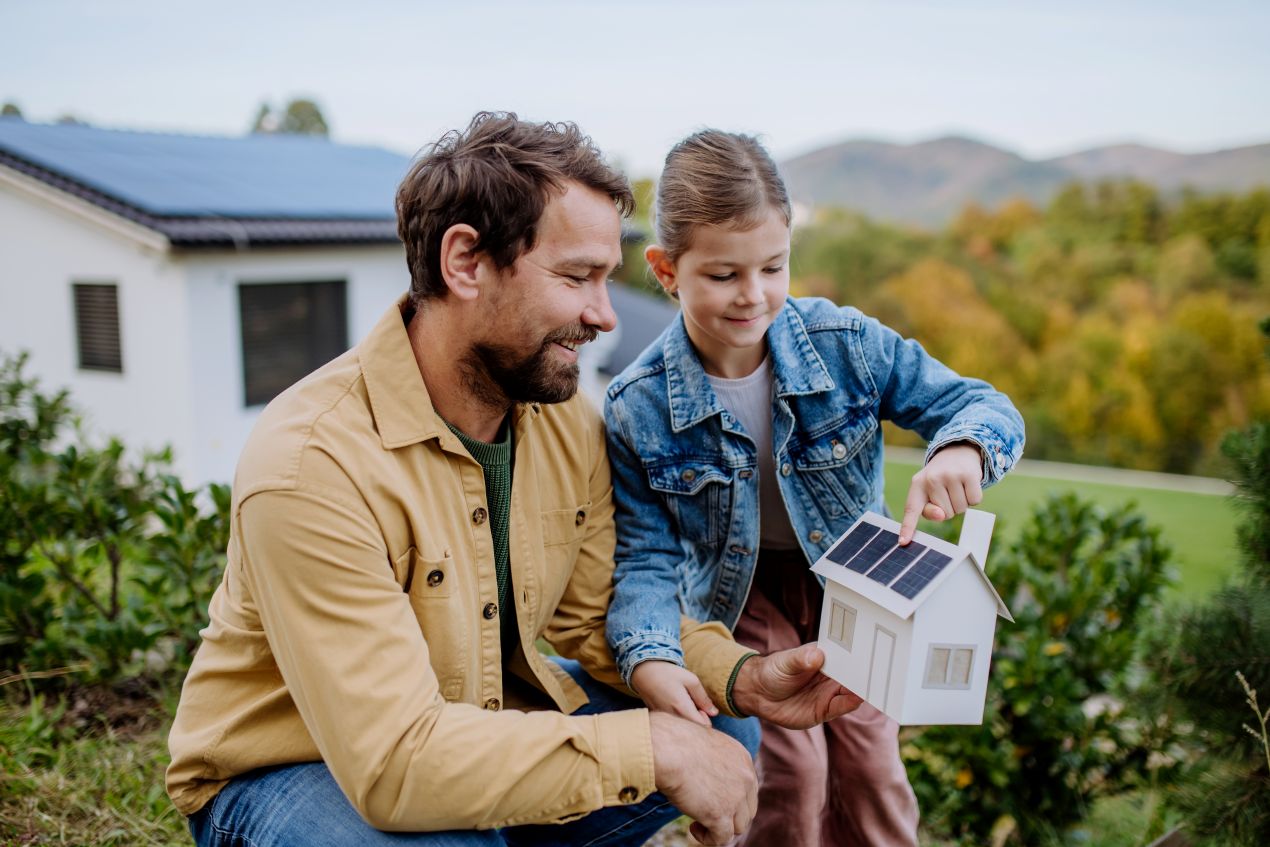 Vater und Tochter in Krefeld betrachten Miniaturhaus mit Photovoltaikanlage Krefeld im Garten