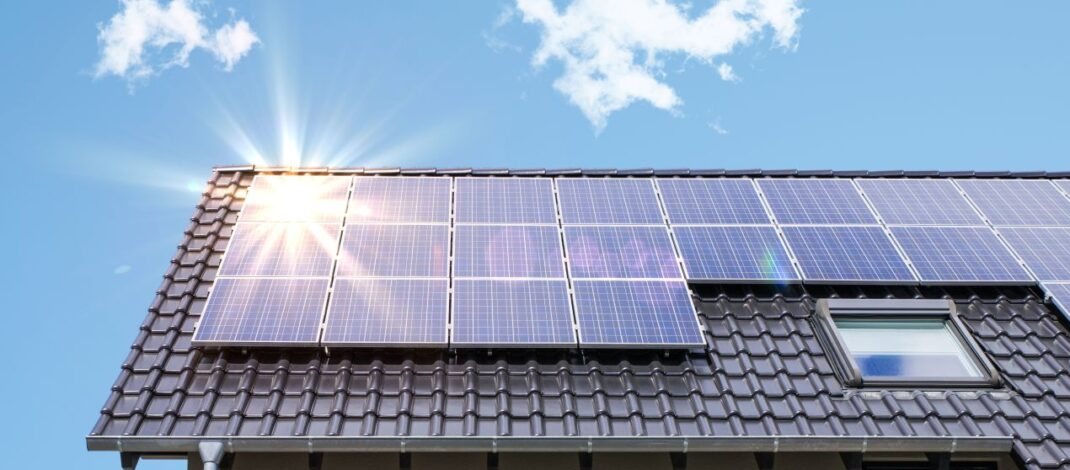 Photovoltaikanlage Krefeld auf einem Schrägdach bei blauem Himmel mit Sonnenreflexion auf den Solarmodulen