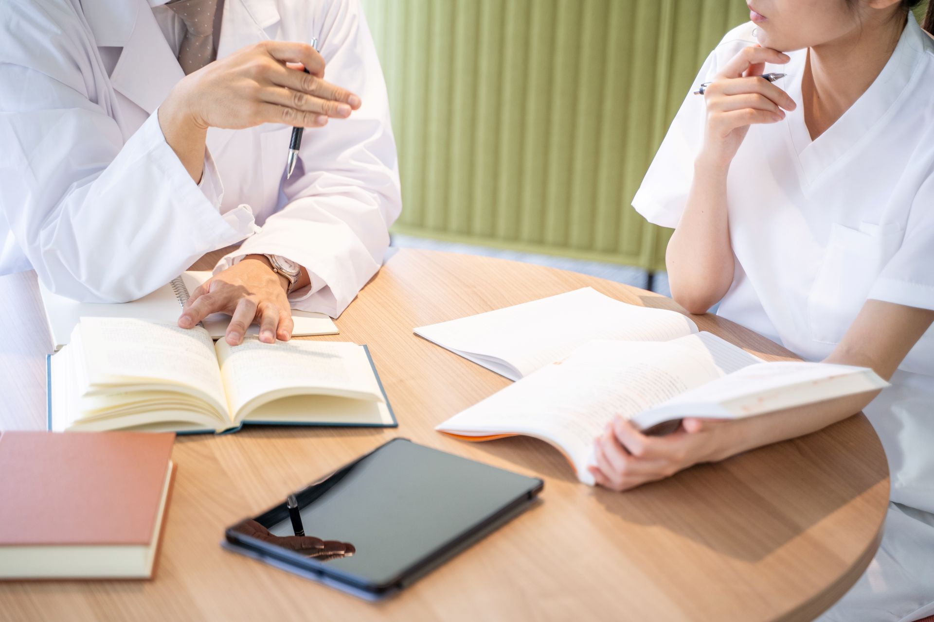 Zwei Personen in weißer Pflegekleidung sitzen mit Fachliteratur am Tisch – typischer Theorie-Unterricht in der Pflegeausbildung